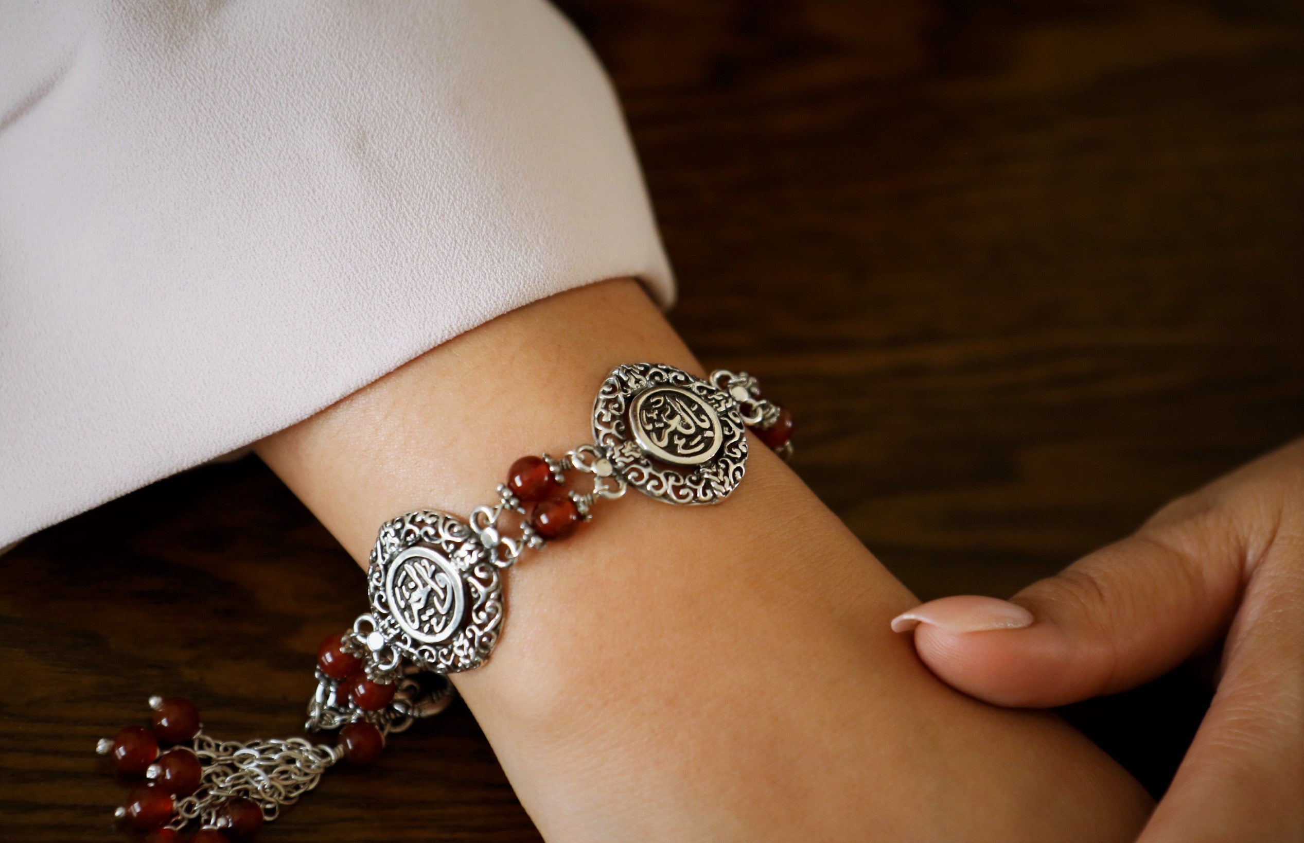 A close-up image of a silver bracelet with Arabic inscriptions and maroon stones, worn on a person's wrist.