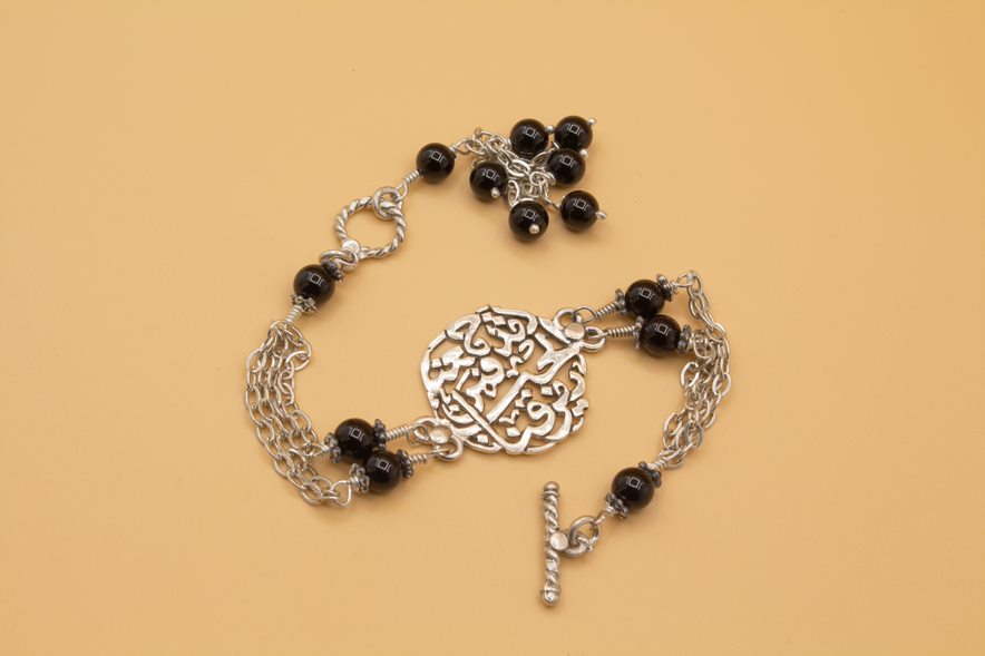 An Arabic silver bracelet with black stones and a silver chain, featuring a quote in silver letters.