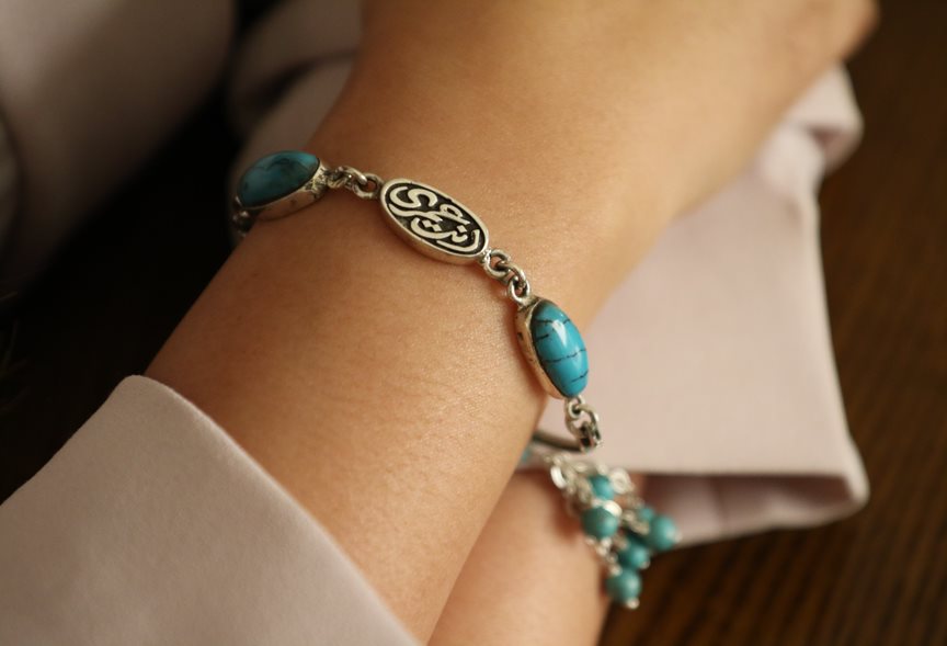 A person's wrist wearing a silver bracelet with turquoise stones and an engraved message 'You are my life'.
