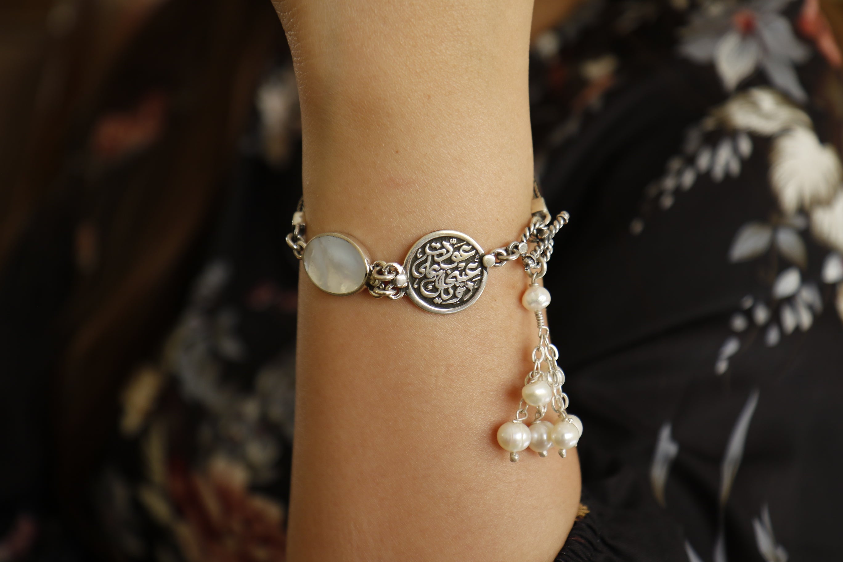 A person is wearing a silver bracelet with a pearl-like bead and floral patterns around the bracelet.