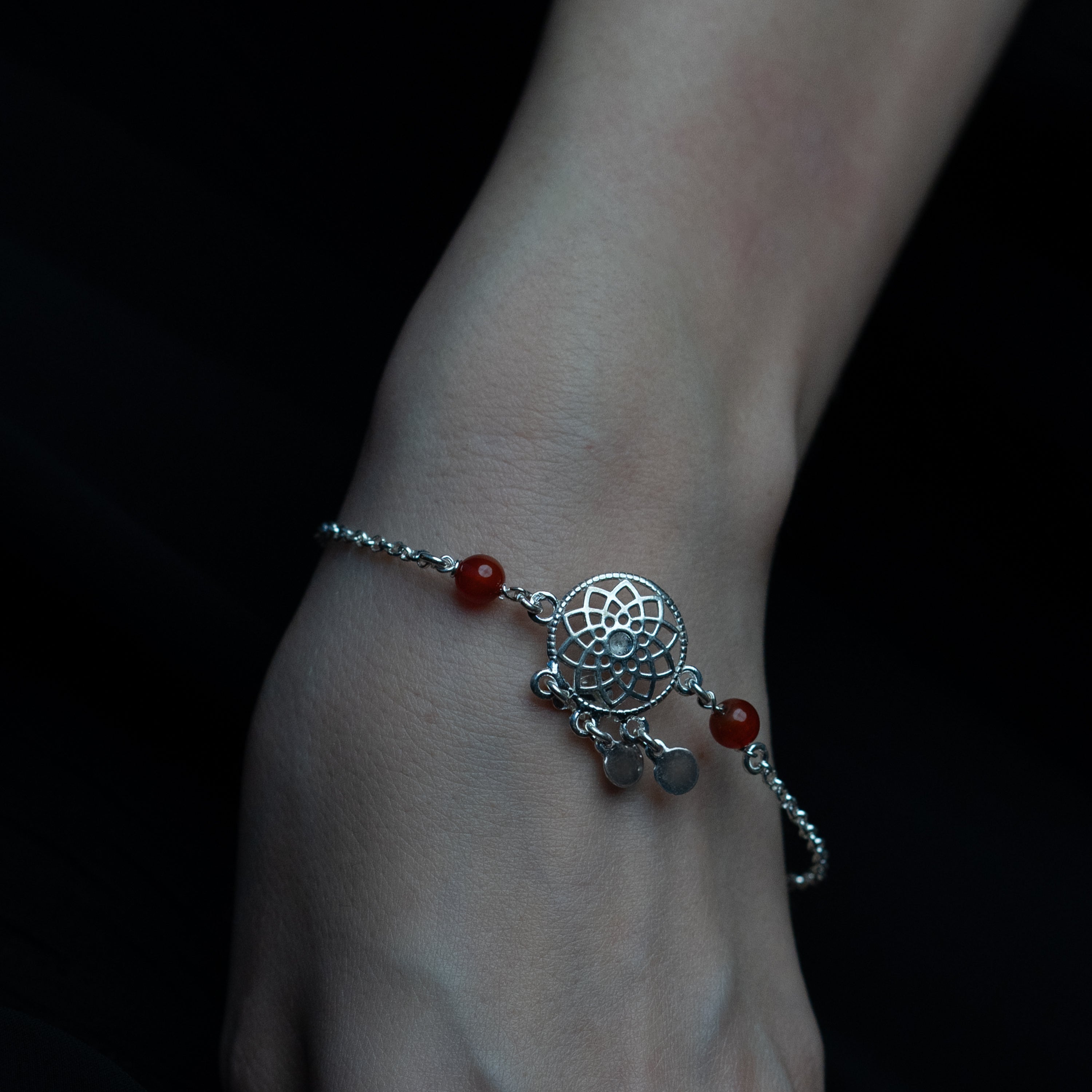A silver bracelet with a star pattern and maroon-colored stones, displayed on a person's wrist.