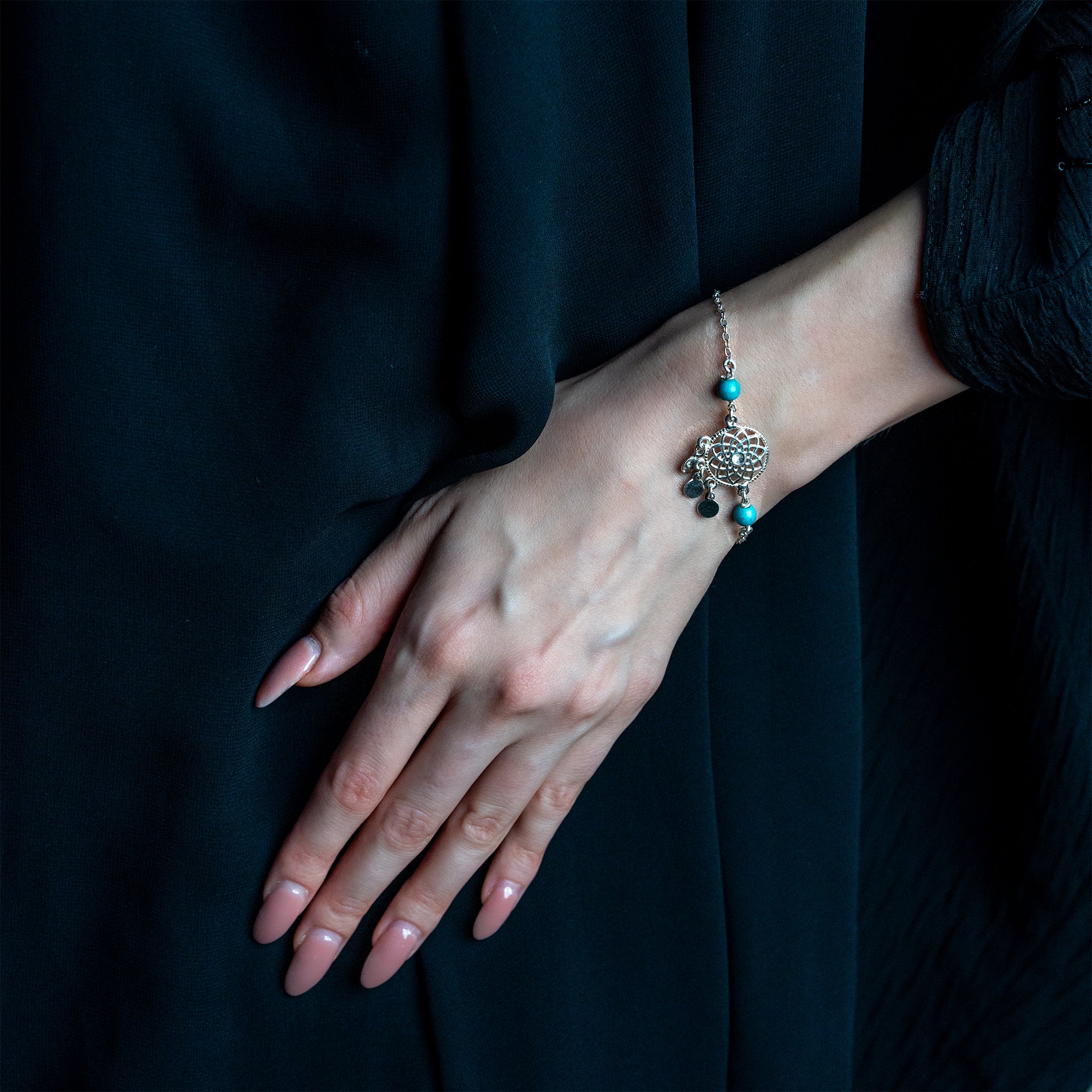 A silver bracelet with turquoise-colored agate stones and star engravings on a person's wrist.