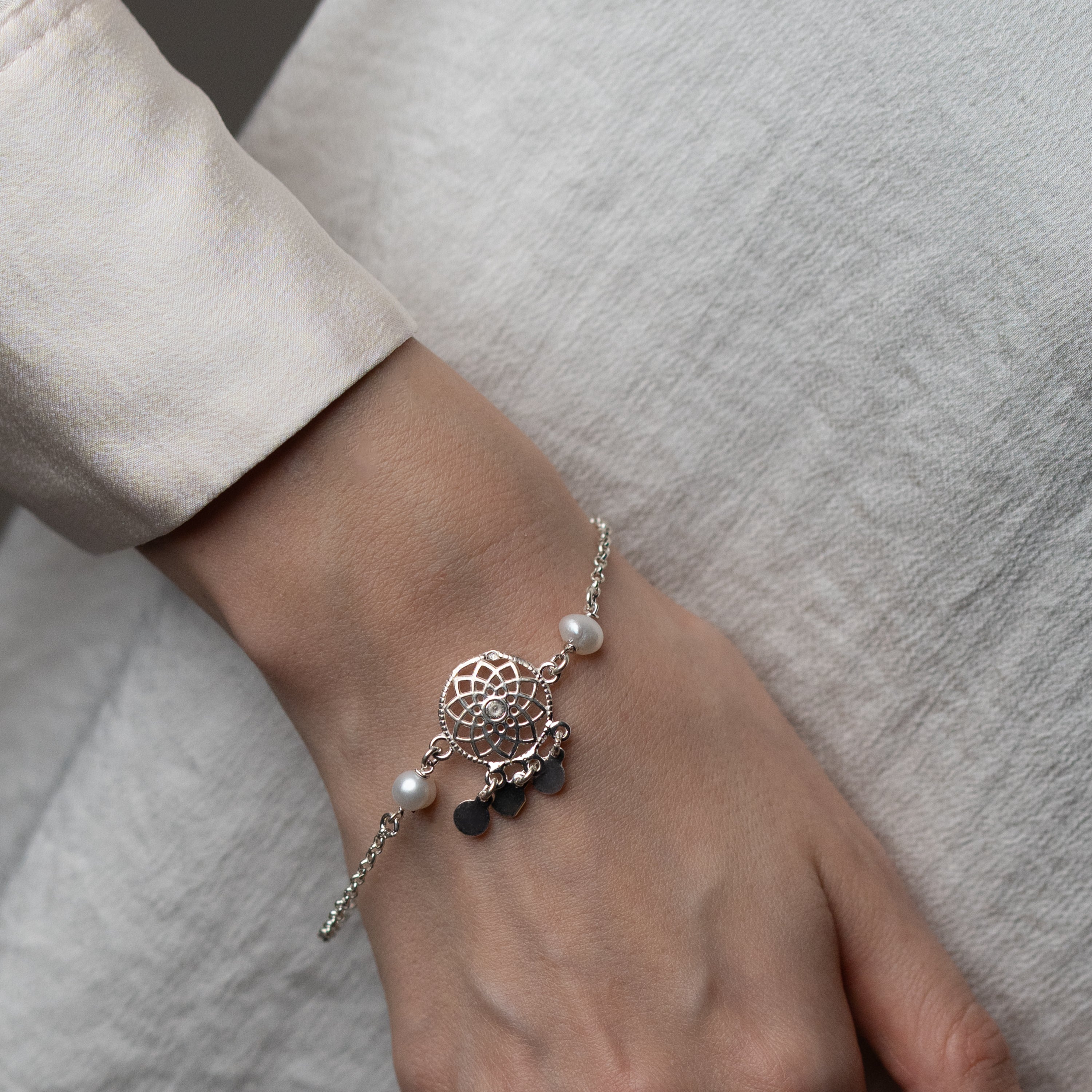A silver bracelet with tangled star engravings and pearl stones, worn on a person's wrist.