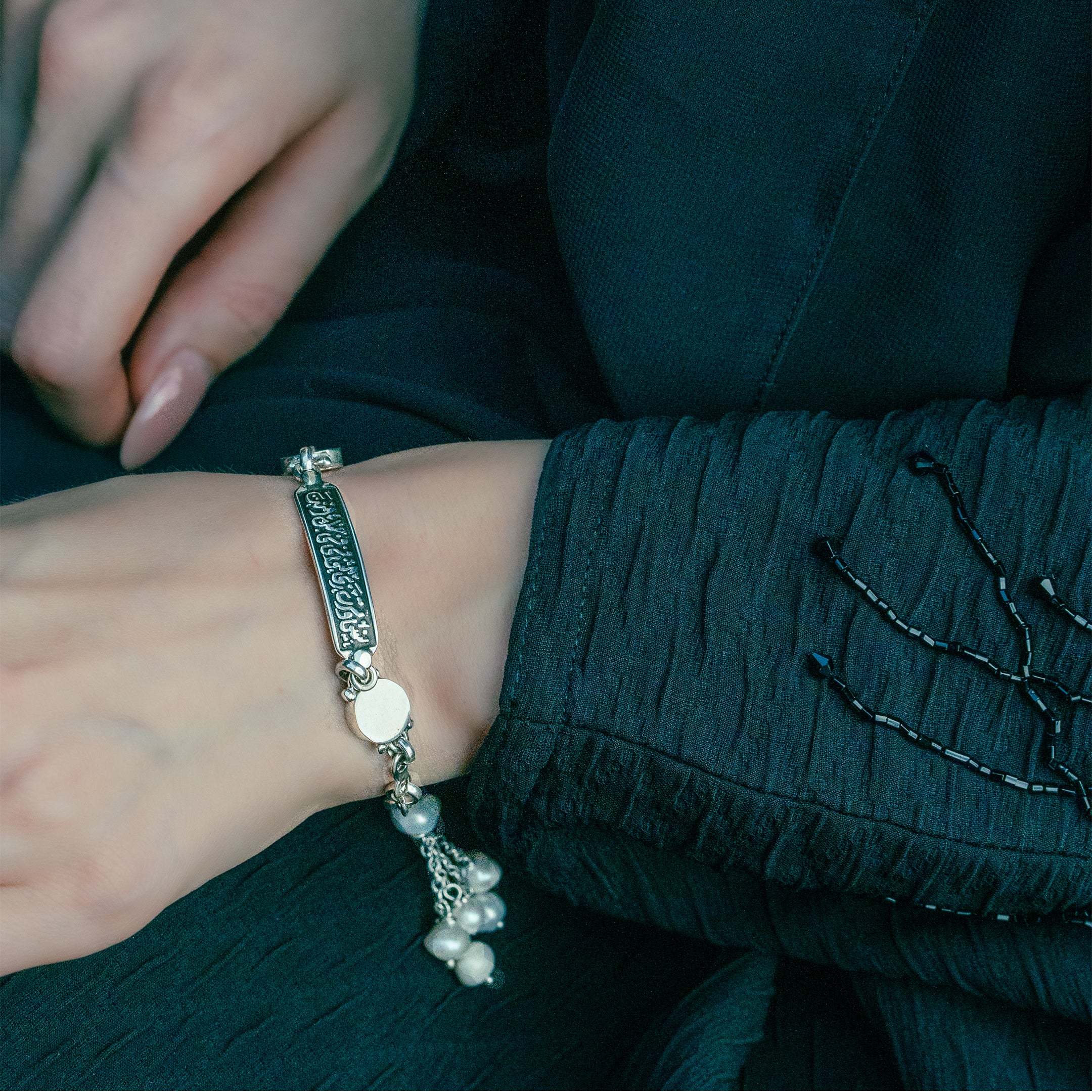 A close-up image of a person's wrist wearing a silver bracelet with a rectangular frame and pearl accents.