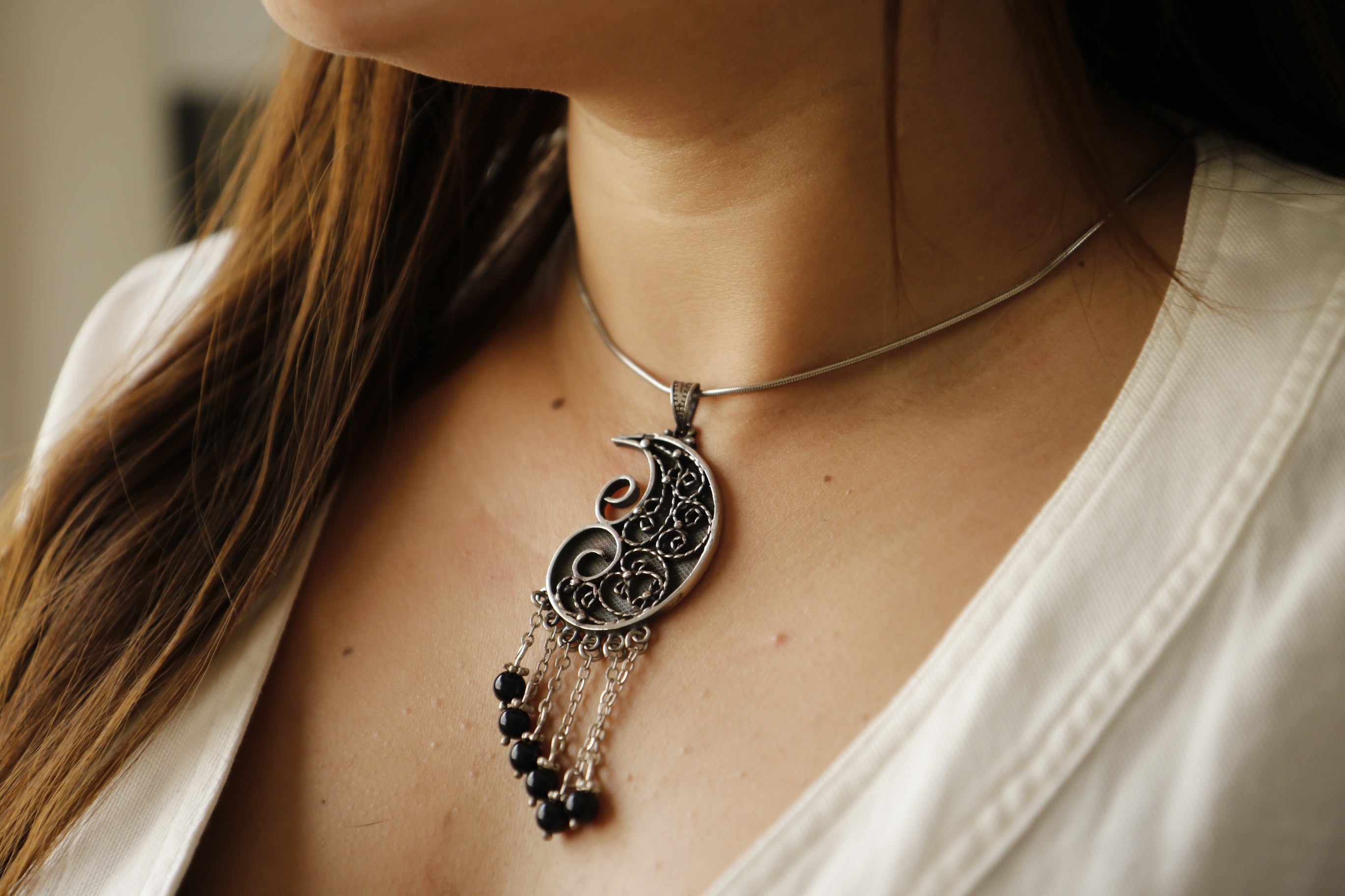 Close-up of a person wearing a silver necklace with black beads