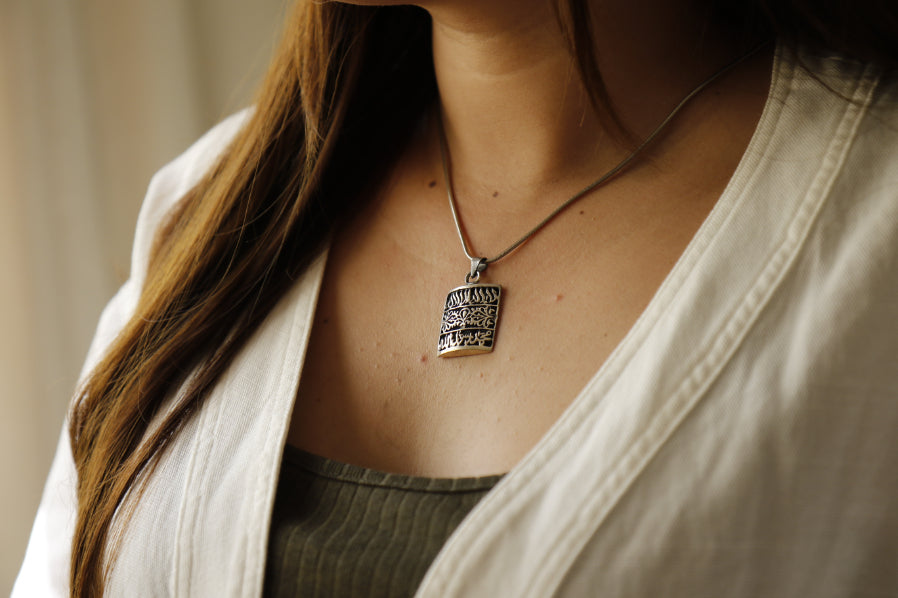 Close-up of a person wearing a necklace with a pendant, blurred background