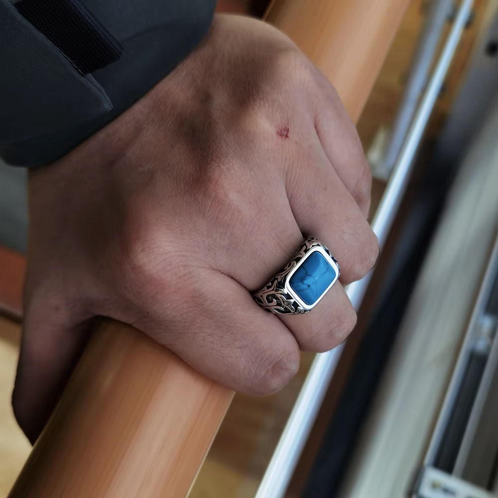 Hand wearing a ring with a blue stone gripping a wooden handle.