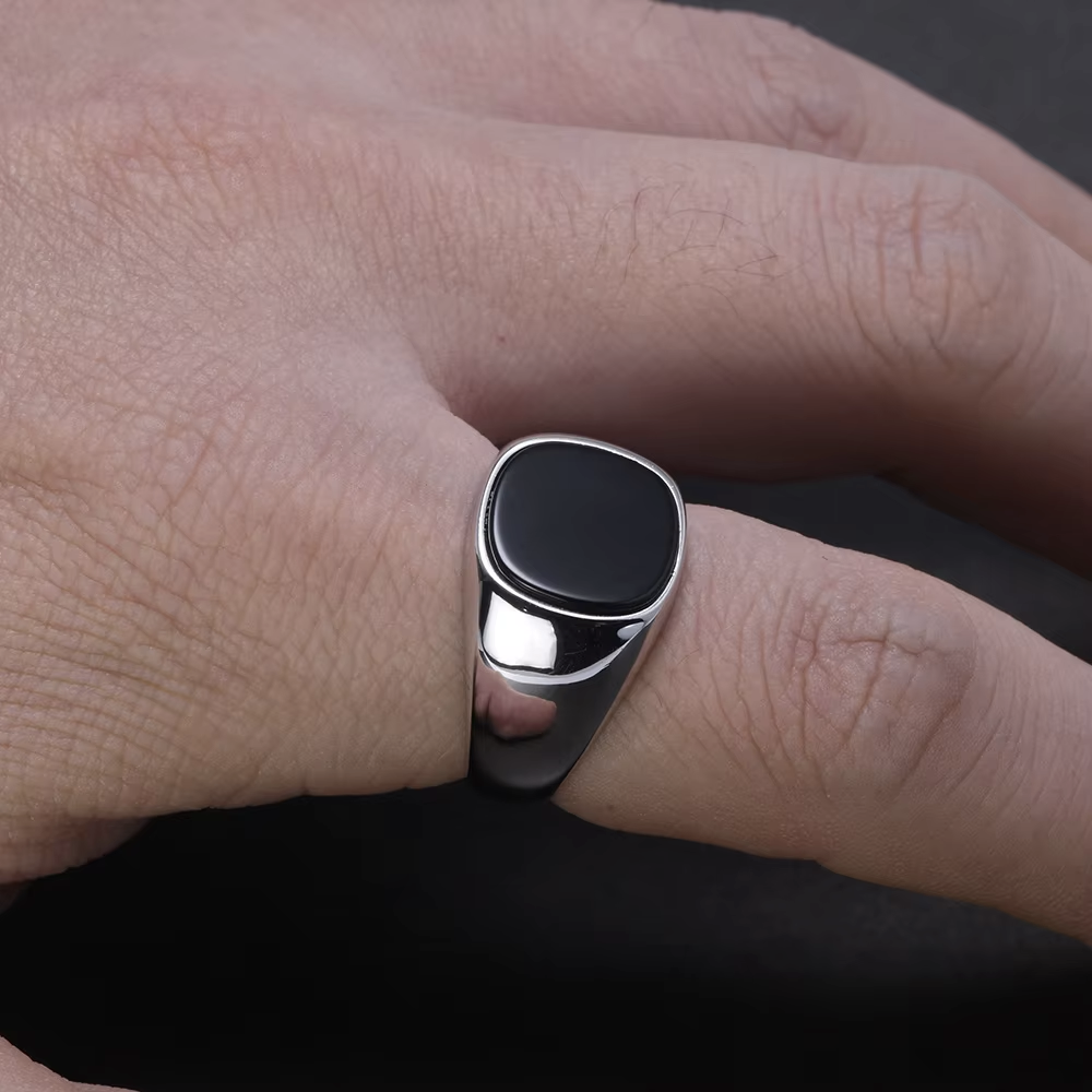 Close-up of a hand wearing a black and silver ring on a dark background