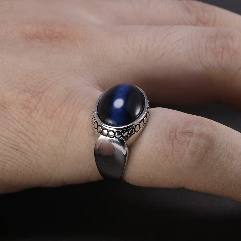 Silver ring with a blue stone on a finger against a dark background