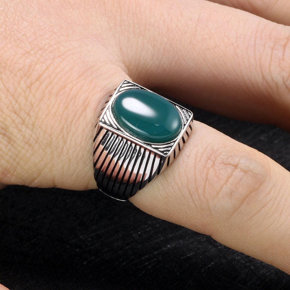 Silver ring with a green stone on a finger against a dark background