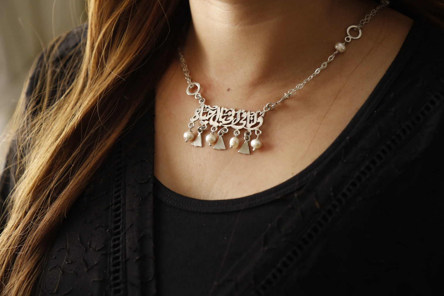A close-up image of a silver chain necklace with pearl beads, worn by a person with a black top and long hair.